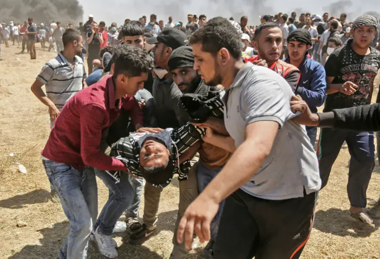 Un Palestinien blessé par des tirs israéliens est évacué par d'autres manifestants, le 14 mai 2018 dans la bande de Gaza, à la frontière avec Israël / © AFP / MAHMUD HAMS