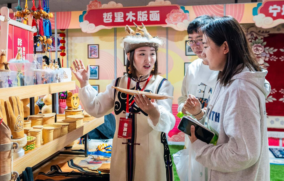 Citizens and tourists learn about the birch bark pyrography making technique of the Oroqen ethnic group at a shopping event for festival goods centered around Chinese intangible cultural heritage (ICH) in north China's Inner Mongolia autonomous region, Jan. 1, 2025. (Photo by Ding Genhou/People's Daily Online)