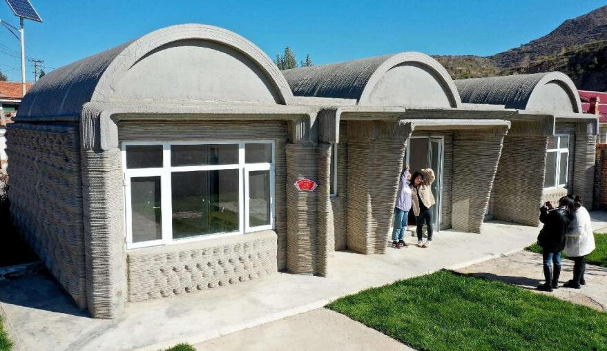 Tourists pose for pictures in front of a 3D-printed farmhouse in Wujiazhuang village, Zhangjiakou, north China's Hebei province. (Photo by Chen Xiaodong/People's Daily Online)